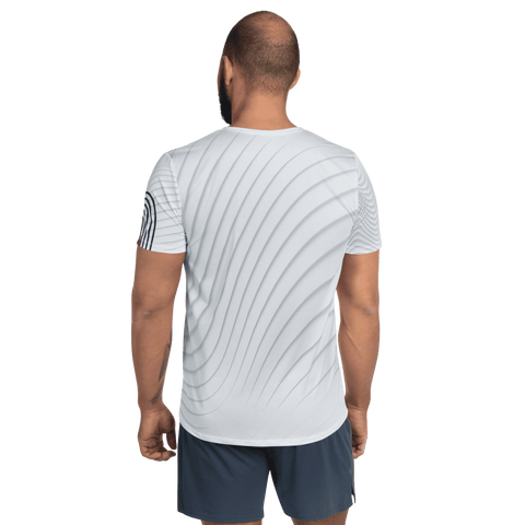 A man with a shaved head stands with his back to the camera, wearing the "A Giant" Men's Athletic T-shirt by magickwear. The shirt is made from four-way stretch sports mesh fabric in a wavy pattern. He pairs it with dark shorts, and his right arm displays a tattoo, while the plain black background enhances his athletic appearance.