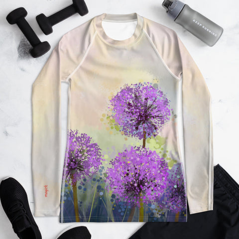 Introducing the "Go Purple" Women's Rash Guard by Magick: a stylish long-sleeve top adorned with a striking design of three large, purple dandelion-like flowers set against a gradient pastel backdrop. The vibrant artwork makes it ideal for active wear. The product image also features black athletic shoes, black shorts, black dumbbells, and a grey water bottle on a white surface, highlighting the perfect ensemble for sports activities and protection with UPF 50+.