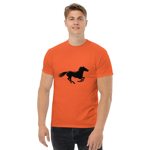 A smiling person wearing Magick's "Onward" Men's Classic Tee, which features a black silhouette of a galloping horse. The 100% cotton, orange T-shirt pairs perfectly with their black pants. They have short, light brown hair and stand against a plain white background, encapsulating casual streetwear outfits.