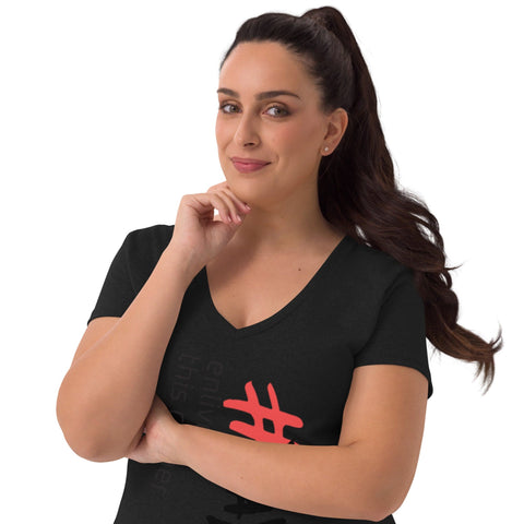 A woman with long dark hair tied back is wearing a Magick "Enliven" Women’s V-neck T-shirt featuring red and white graphics. She stands against a plain background, slightly smiling, with one hand thoughtfully touching her chin.