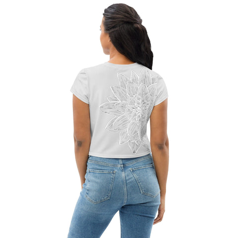 A woman with long, dark hair stands facing away from the camera, wearing a casual "Magnificence" crop tee by magickwear, featuring an oversized floral design on the back and light blue jeans. Her stylish wardrobe choice gives her a contemporary yet relaxed look.