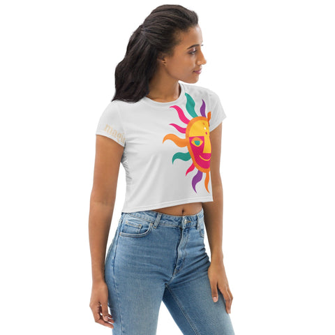 A woman with long dark hair is wearing the stylish "Magnificence" Crop Tee by magickwear, featuring a vibrant sun graphic with colorful rays and a smiling face. She is looking to her left and also wearing high-waisted blue jeans against a plain white background.