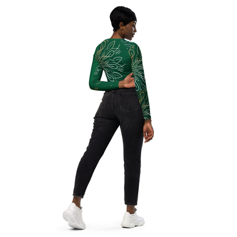 Facing away, a person wears the "Proud of Me" long-sleeve crop top by magickwear, featuring a white floral pattern on green, paired with black jeans and white sneakers. Their left hand is raised behind their back while the right rests at their side against a plain white backdrop—an eco-friendly style choice.