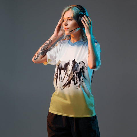 A person with tattoos on their arms is standing while wearing a headset and magickwear's "Life is Playground" recycled unisex sports jersey, which features a striking black and white horse design. They are adjusting the headset and looking to the side. The lighting has a cool tone, and they are in a casual setting.