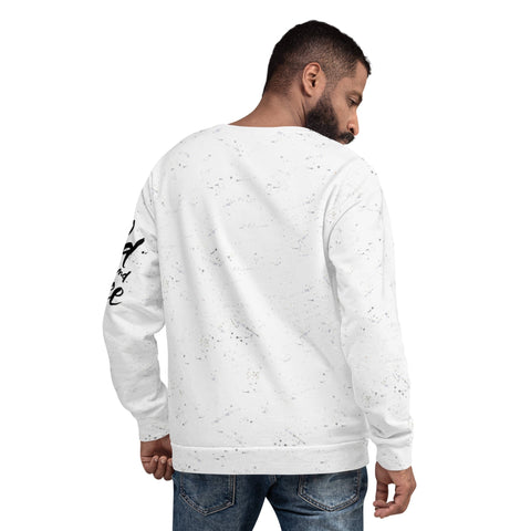 A man with short dark hair and a beard is facing away, revealing the back of his stylish "Wild & Free" Unisex Sweatshirt from magickwear. The white sweatshirt features speckles and has text on the left sleeve. He pairs it with blue jeans against a plain white background.