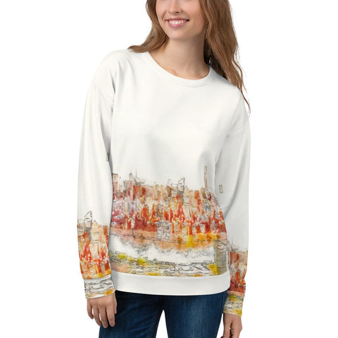 A woman with long hair is smiling while wearing a stylish and comfortable "Dreamscape" Unisex Sweatshirt from magickwear, adorned with an all-over print of a vibrant cityscape design on the lower half and sleeves. She pairs it with blue jeans and stands against a plain background.