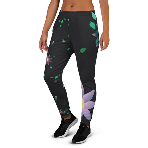 A person wearing magickwear's stylish "Better Universe" Women's Joggers in a floral-patterned black design and black sneakers stands with hands relaxed at the sides. These women's joggers feature a comfortable fit, adorned with purple and green flower designs against a plain white background.