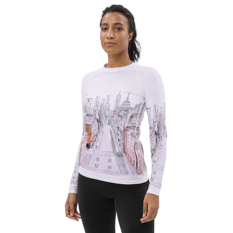 A person wearing the magickwear "MY NYC" Women's Rash Guard, featuring a cityscape design on the front, stands against a plain white background. They have dark hair pulled back and are also wearing black pants. The individual is facing forward with a neutral expression.