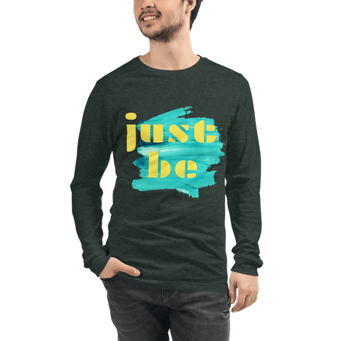A person wearing the "Just Be ..." Unisex Lettering Tee by magickwear stands against a plain background with a hand casually tucked in their pocket. This dark green tee, featuring the words "just be" in yellow and blue font on the front, complements their laid-back style effortlessly.