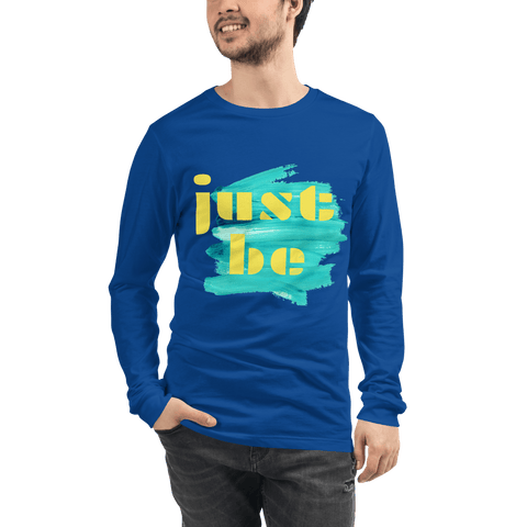A person wearing the "Just Be ..." Unisex Lettering Tee from magickwear, showcasing the phrase "just be" in yellow on a turquoise paint stroke. They have dark hair, a short beard, and are posing with one hand in their pocket. This comfortable and durable shirt is ideal for any occasion.