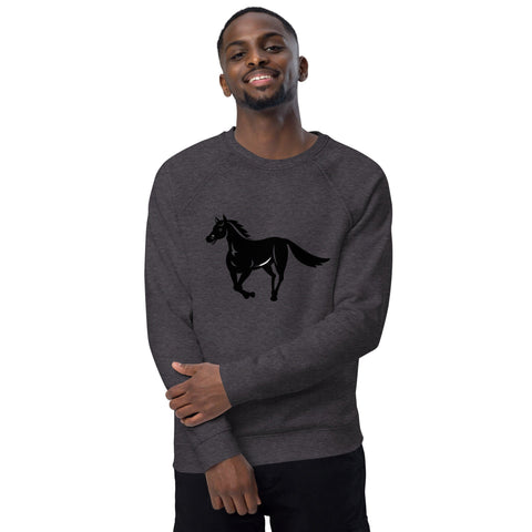 A person with short hair is smiling confidently at the camera, dressed in magickwear's "A Horse's Kingdom" Unisex Organic Raglan Sweatshirt, which features a black horse graphic on the chest. They are standing against a plain white background, showcasing the comfort of its brushed fleece lining and 100% organic cotton.