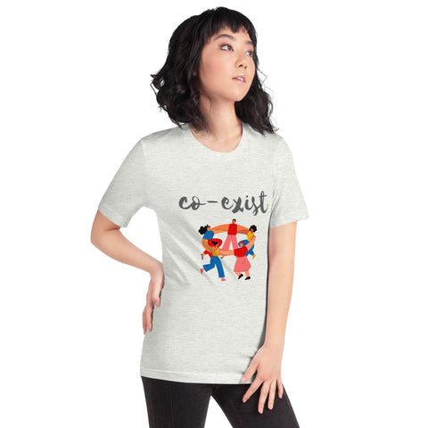 A person with shoulder-length dark hair is wearing a stylish magickwear "Co-exist" Short-Sleeve Unisex T-Shirt that features an illustration of diverse figures holding hands in a circle. The light-colored t-shirt stands out as the person, with one hand on their hip, gazes off to the side.