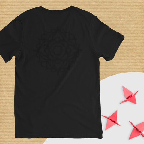 The "At Ease" Unisex Short Sleeve V-Neck T-Shirt by magickwear showcases a black design with a subtle circular pattern on a textured background. This fashion-conscious piece features three red origami cranes meticulously placed on the lower right, all crafted from soft combed cotton and resting against a pristine white surface.