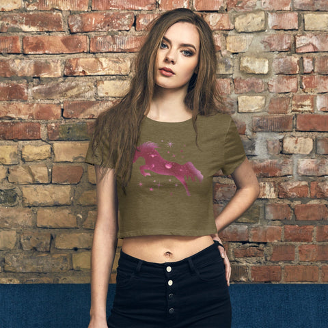 A person with long hair poses confidently in front of a brick wall, showcasing a trendy garment: the "M Moment" Women’s Crop Tee by magickwear, featuring a pink unicorn design, paired seamlessly with dark high-waisted jeans.