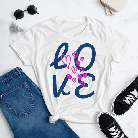 The magickwear "LOVE Big" Women's Short Sleeves T-shirt, made of 100% pre-shrunk cotton, sports bold blue "Love" lettering with pink hearts. It's styled on a marble surface with dark blue jeans, black sneakers, sunglasses, and a beige bag for an effortlessly charming look.