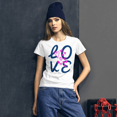 A woman leans against a charcoal wall in a classic fit, 100% cotton magickwear "LOVE Big" Women's Short Sleeve Lettering T-shirt with pink hearts. Paired with jeans and a navy beanie, she stands stylishly beside chains. This pre-shrunk tee ensures the perfect fit every time.